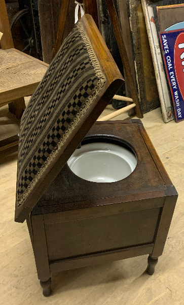 wooden cupboard with a lifted padded top showing a white toilet bowl inside